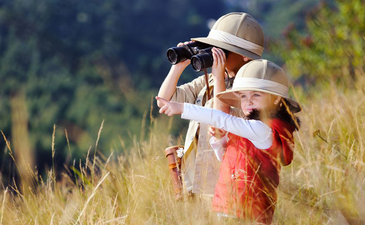 Children brother and sister playing outdoors pretending to be on safari and having fun together with binoculars and hats @Warren Goldswain